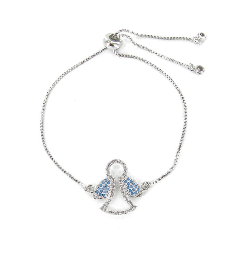 May include: A silver adjustable bracelet with a small angel charm. The angel's wings are decorated with blue crystals.