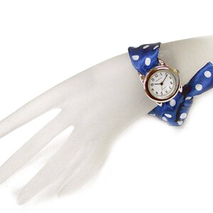 May include: A blue and white polka dot fabric watch band with a silver watch face. The watch face has black numbers and hands.