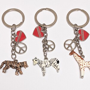 May include: Three silver keychains with red heart charms, peace sign charms, and animal charms. One keychain has a tiger charm, one has a zebra charm, and one has a giraffe charm.