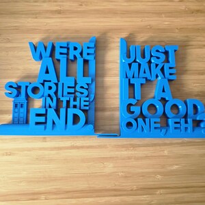 May include: A pair of blue bookends, each with a quote from a popular science fiction show. The left bookend features a TARDIS design. The text reads "WE'RE ALL STORIES IN THE END" and "JUST MAKE IT A GOOD ONE, EH?".