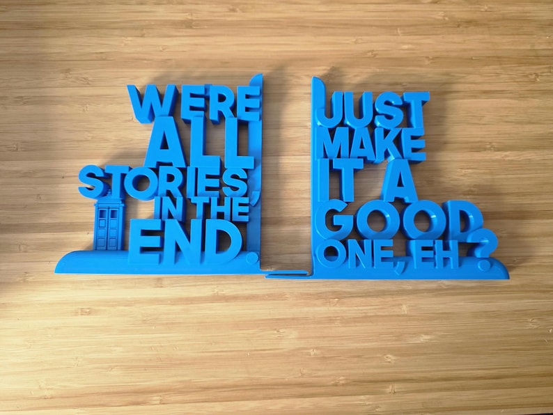 May include: A pair of blue bookends, each with a quote from a popular science fiction show. The left bookend features a TARDIS design. The text reads "WE'RE ALL STORIES IN THE END" and "JUST MAKE IT A GOOD ONE, EH?".