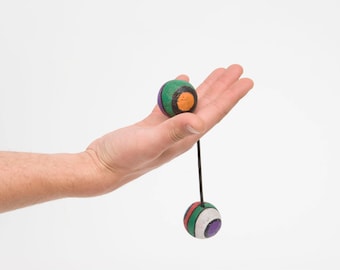 May include: A hand holds a string with two colorful balls attached. The balls are green, orange, purple, and white.