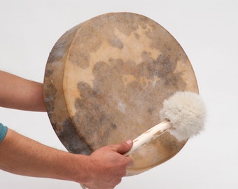 May include: A person holding a brown leather drum with a white fur beater. The drum is being played with the beater.