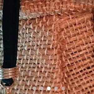 May include: A close-up of a brown burlap bag with a black strap and a silver charm. The strap has a silver ring around it.