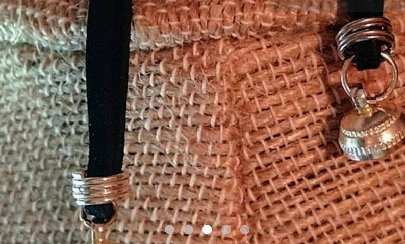 May include: A close-up of a brown burlap bag with a black strap and a silver charm. The strap has a silver ring around it.