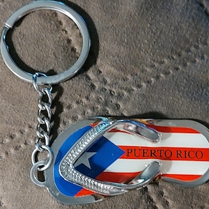 May include: A silver keychain shaped like a flip-flop with the Puerto Rican flag and the text "PUERTO RICO" on it.