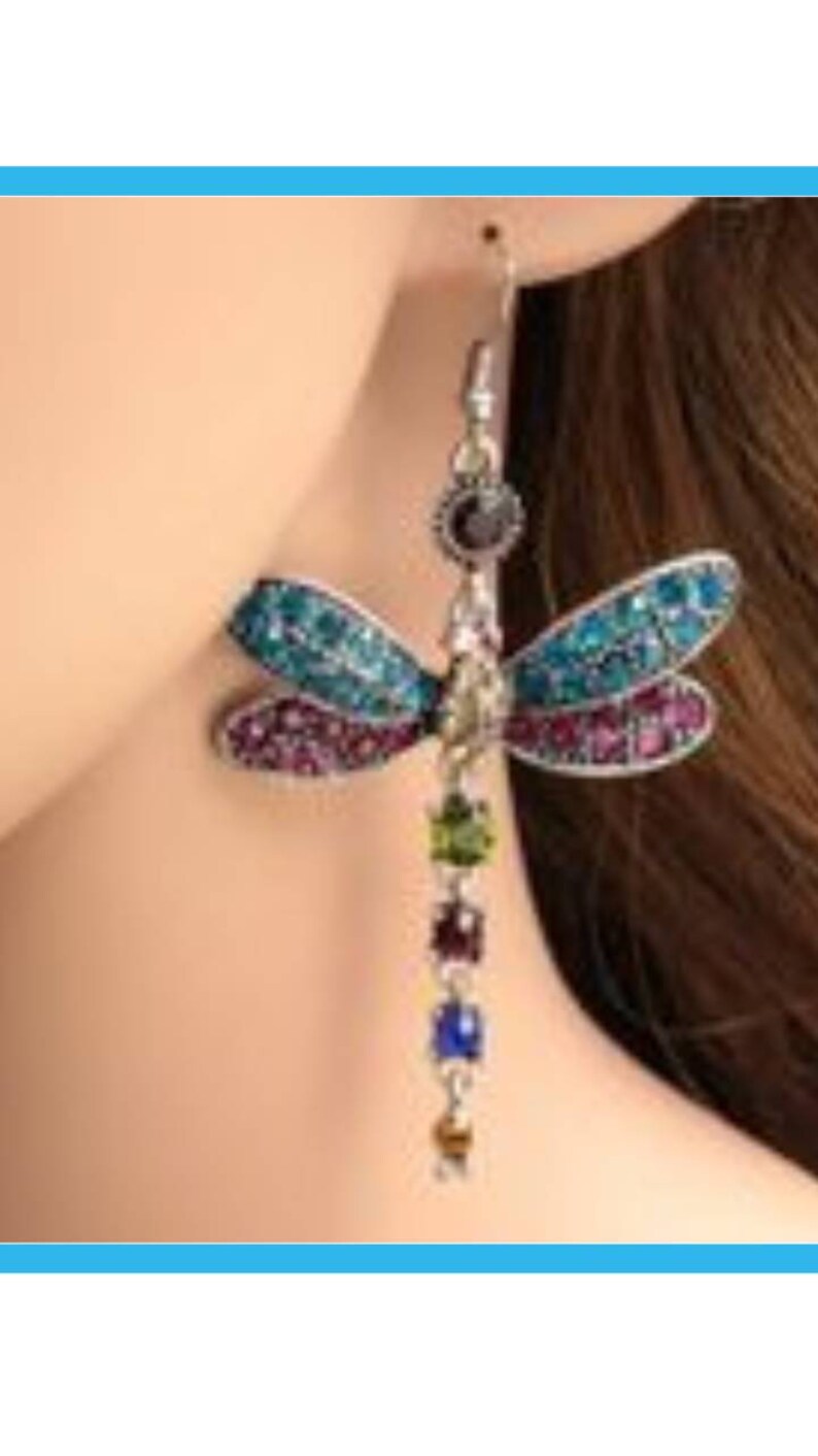 May include: A pair of dangle earrings featuring a dragonfly design with blue, green, and purple rhinestones. The dragonfly is attached to a chain with colorful beads.