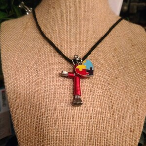 May include: A red horseshoe cross necklace with a blue, yellow and red puzzle piece heart charm on a black cord.