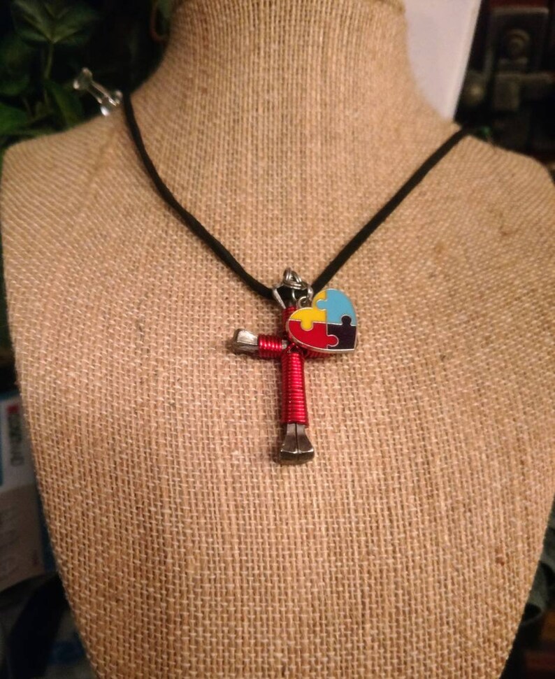 May include: A red horseshoe cross necklace with a blue, yellow and red puzzle piece heart charm on a black cord.