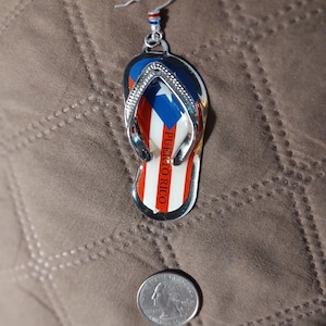 May include: Silver earring with a flip-flop charm featuring the Puerto Rican flag and the text "PUERTO RICO".