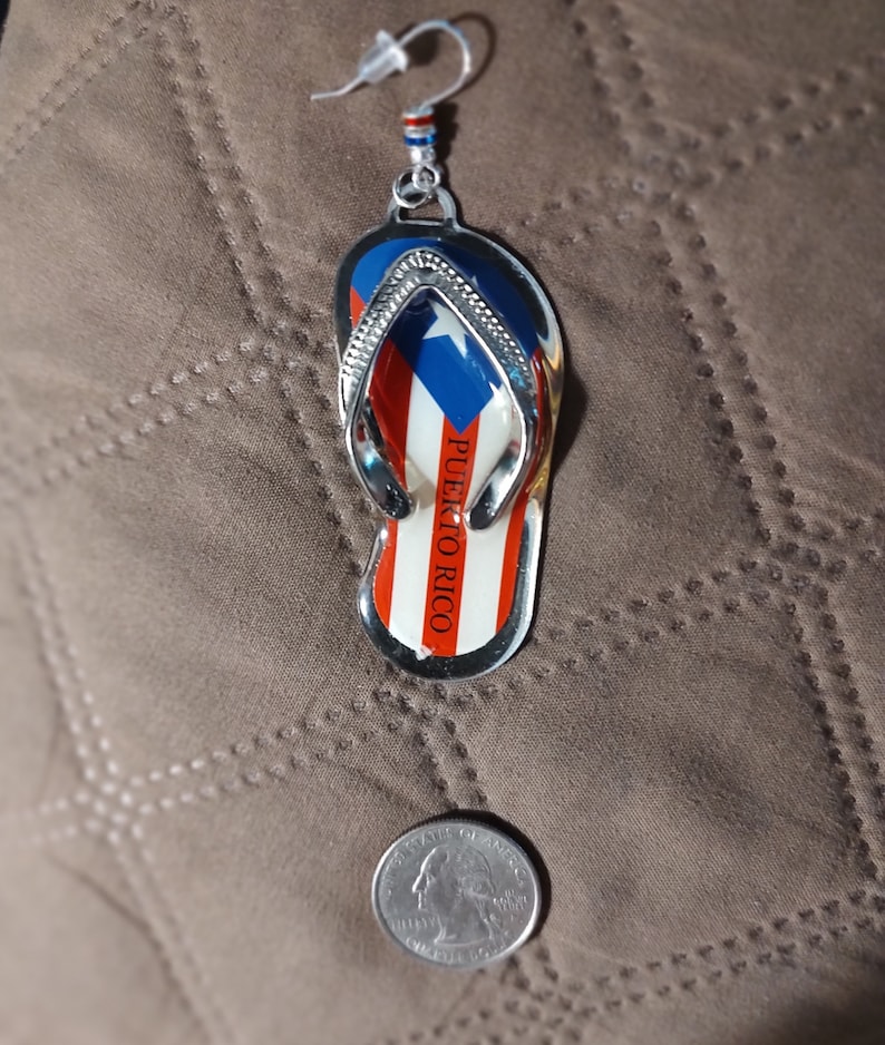 May include: Silver earring with a flip-flop charm featuring the Puerto Rican flag and the text "PUERTO RICO".