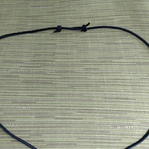 Op de afbeelding: Een zwarte leren koordsnoer met een zilveren hart hanger.