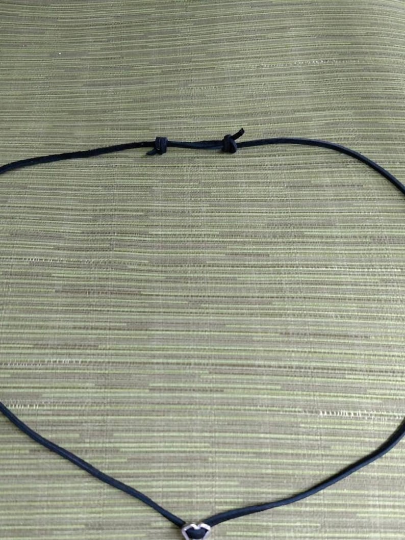 Op de afbeelding: Een zwarte leren koordsnoer met een zilveren hart hanger.