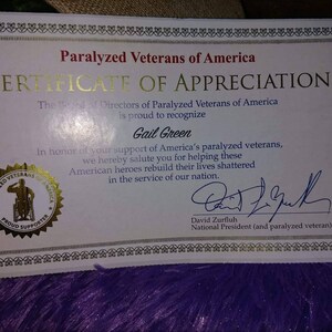 Puede incluir: Un certificado de agradecimiento de Paralyzed Veterans of America, presentado a Gail Green por apoyar a los veteranos paralizados. El certificado presenta un sello dorado con una persona en silla de ruedas y el texto "Paralyzed Veterans of America Proud Supporter". El certificado est&aacute; firmado por David Zurfluh, presidente nacional (y veterano paralizado).