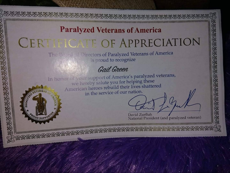 Puede incluir: Un certificado de agradecimiento de Paralyzed Veterans of America, presentado a Gail Green por apoyar a los veteranos paralizados. El certificado presenta un sello dorado con una persona en silla de ruedas y el texto "Paralyzed Veterans of America Proud Supporter". El certificado est&aacute; firmado por David Zurfluh, presidente nacional (y veterano paralizado).