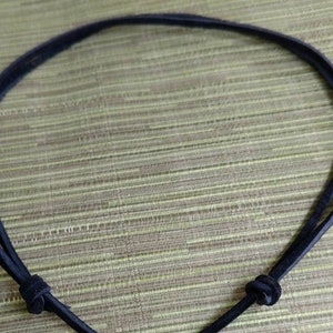Op de afbeelding: Een zwarte leren koordsnoer met een zilveren hartvormige hanger.