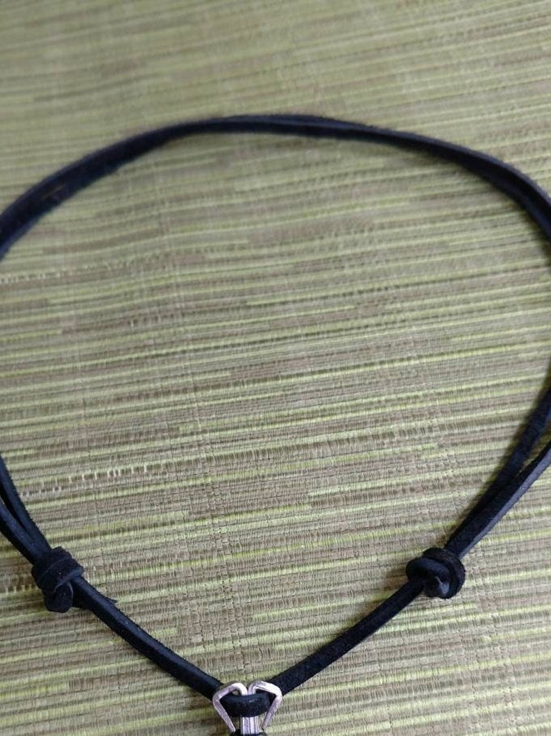 Op de afbeelding: Een zwarte leren koordsnoer met een zilveren hartvormige hanger.