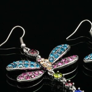 May include: A pair of silver dragonfly earrings with colorful rhinestones. The dragonflies have blue, pink, and green wings with a clear rhinestone body.
