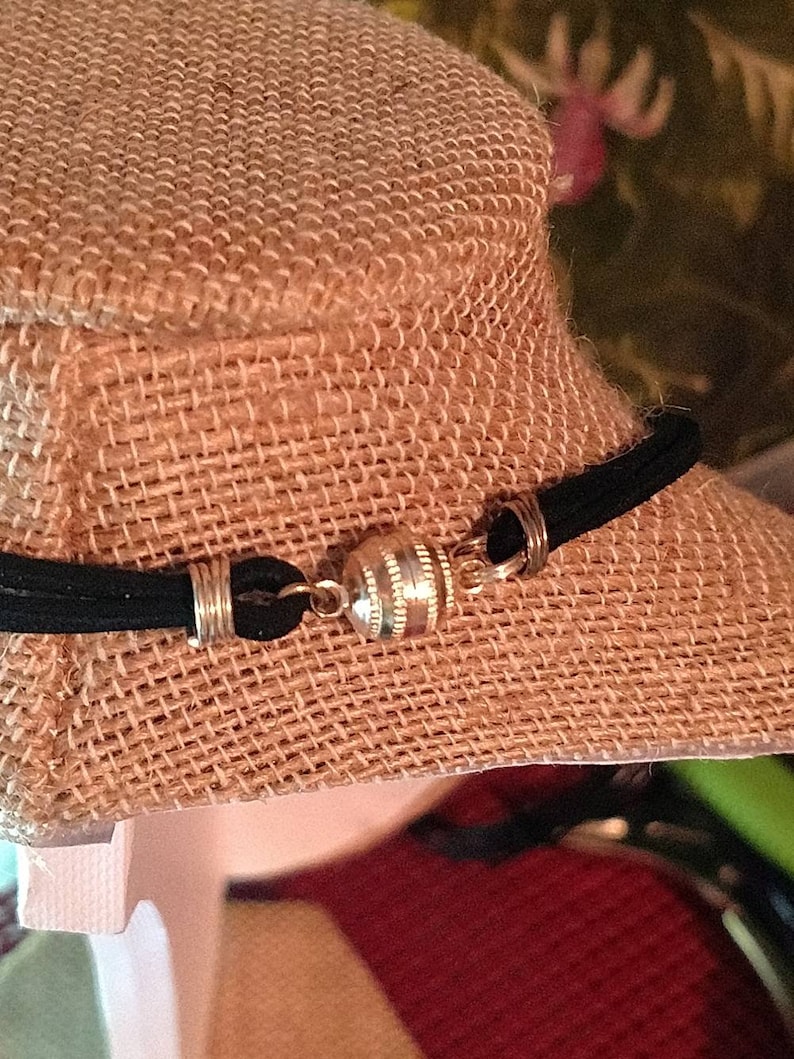 May include: A black necklace with a magnetic clasp, displayed on a burlap-covered bust. The clasp is silver and cylindrical, connecting the ends of the necklace. The necklace appears to be made of a black, suede-like material.
