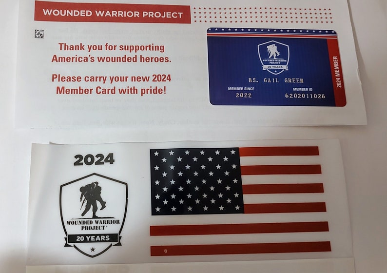Op de afbeelding: Een witte kaart met het Wounded Warrior Project-logo en de tekst "20 Years". De kaart heeft ook een zwart-witte Amerikaanse vlag.