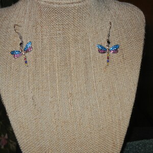 May include: A pair of dangle earrings featuring a dragonfly design with blue, pink, and multi-colored accents.