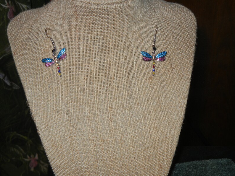 May include: A pair of dangle earrings featuring a dragonfly design with blue, pink, and multi-colored accents.