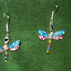 May include: A pair of silver dragonfly earrings with blue, pink, and rainbow colored rhinestones.