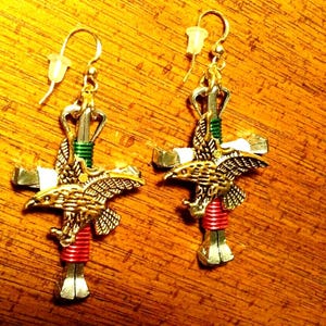 May include: A pair of silver and gold earrings featuring a cross with a red, green, and white wrapped nail, topped with a golden eagle.