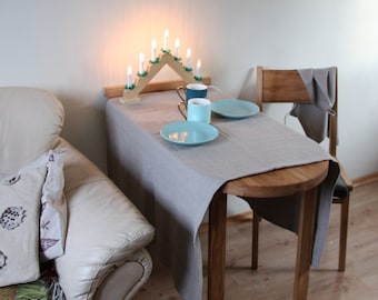 Könnte beinhalten: Ein kleiner Tisch mit einer grauen Tischdecke, gedeckt für zwei Personen mit zwei blauen Tassen und zwei blauen Tellern. Ein Kerzenhalter aus Holz mit brennenden Kerzen steht auf dem Tisch. Ein weißes Sofa mit einer Wolldecke ist im Hintergrund.