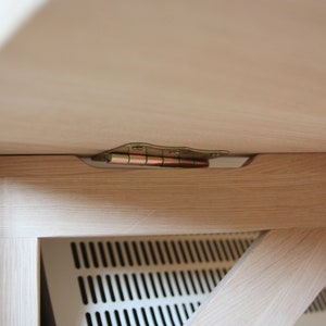 May include: Close-up of a wooden table with a metal hinge connecting the tabletop to the base. The hinge is visible from underneath the table.