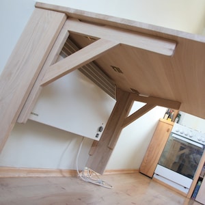 May include: A wooden table with a white electric heater mounted underneath. The table is made of light wood and has a simple design. The heater is a standard model with a white finish.