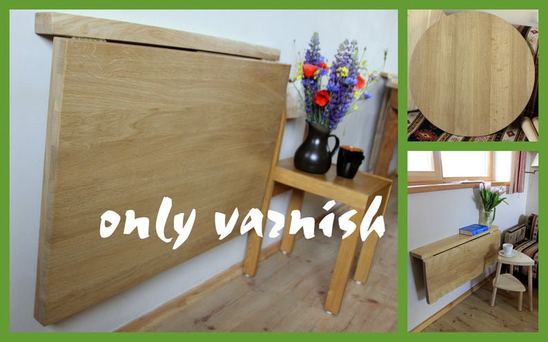 May include: A wooden folding wall table with a light wood finish. The table is mounted to a wall and folds down to save space. The table is shown in two different rooms, one with a vase of flowers and a chair, and the other with a book and a small stool.