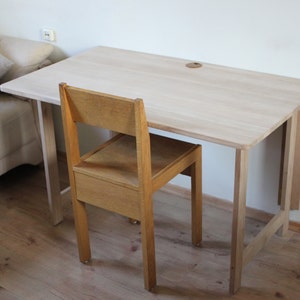 May include: A light wood folding desk with a natural finish and a matching wooden chair. The desk is attached to a wall and has a simple design.