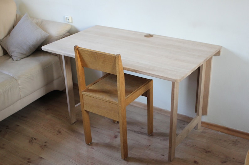 May include: A light wood folding desk with a natural finish and a matching wooden chair. The desk is attached to a wall and has a simple design.
