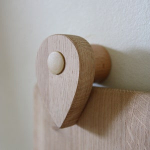 May include: A wooden wall-mounted hook with a teardrop-shaped design and a round knob. The hook is made of light-colored wood and has a natural finish.