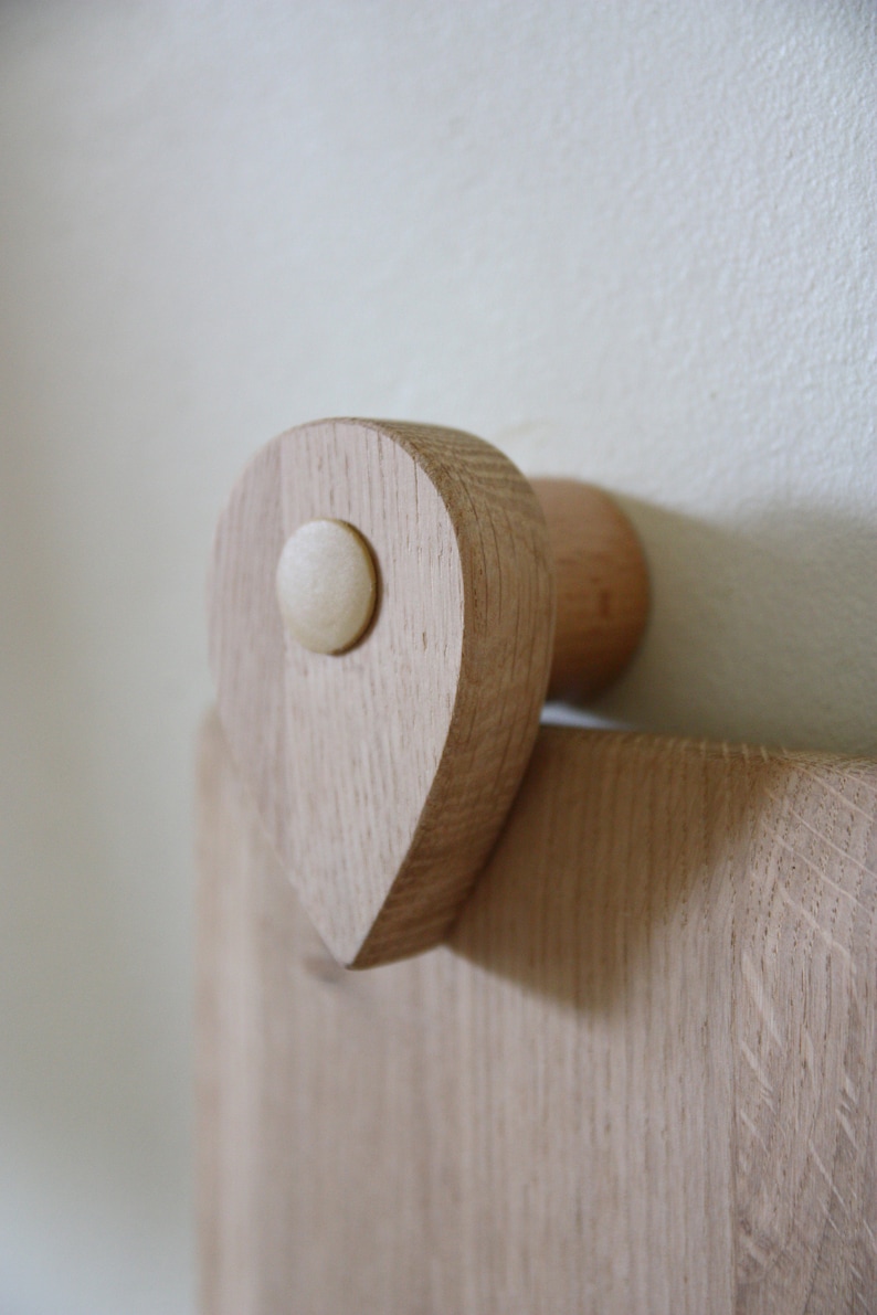 May include: A wooden wall-mounted hook with a teardrop-shaped design and a round knob. The hook is made of light-colored wood and has a natural finish.