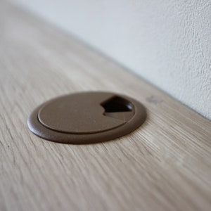 May include: A close-up of a brown plastic cord cover on a light wood surface.