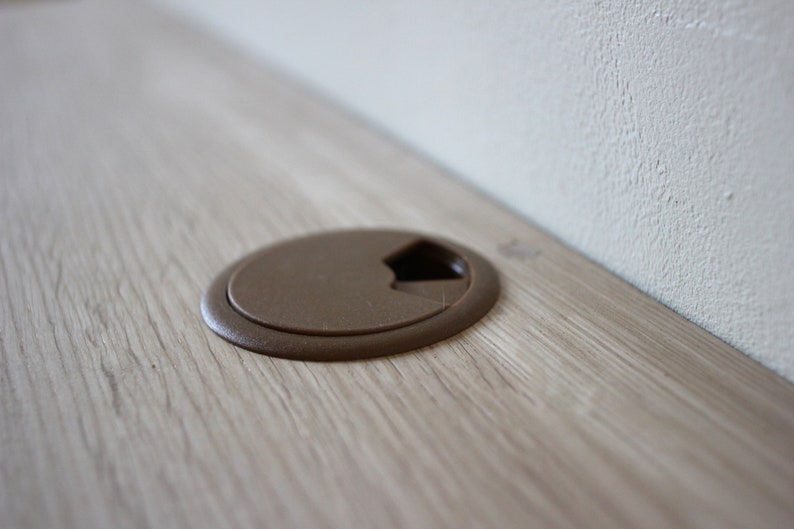 May include: A close-up of a brown plastic cord cover on a light wood surface.
