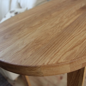 May include: A close-up of a round wooden table top with a natural wood finish. The table top is smooth and has a light brown color.