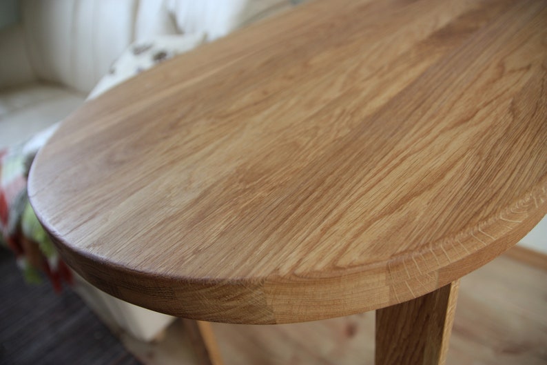 May include: A close-up of a round wooden table top with a natural wood finish. The table top is smooth and has a light brown color.