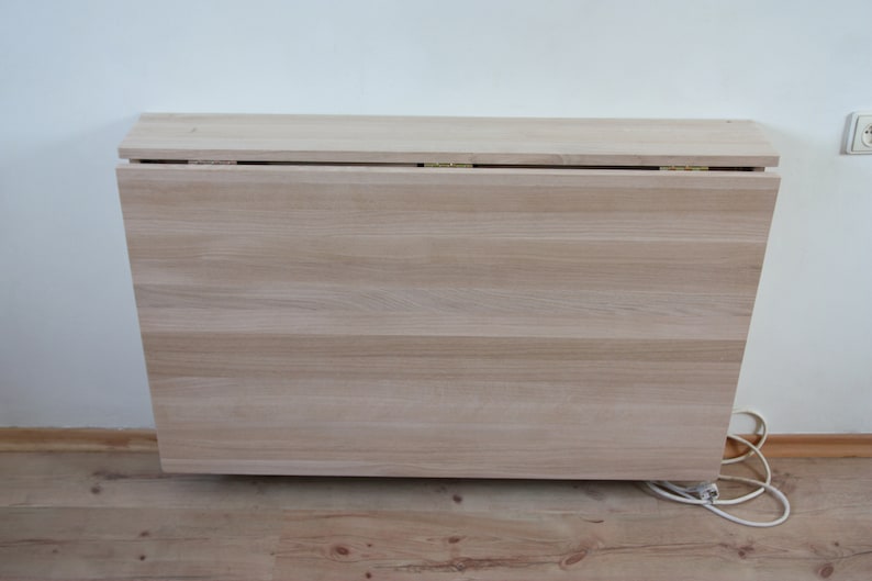 May include: A light wood folding table with a white top and a white wall in the background.