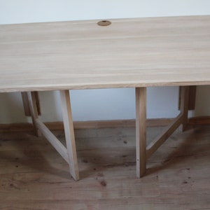 May include: A light wood folding table with a simple design. The table has a rectangular top and a set of four legs that fold in for storage.