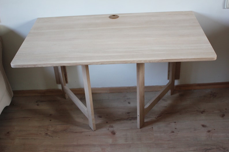 May include: A light wood folding table with a simple design. The table has a rectangular top and a set of four legs that fold in for storage.