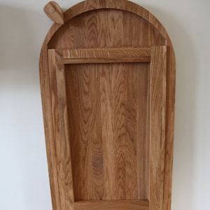May include: A wooden folding table with an arched top. The table is made of light brown wood and has a simple design.