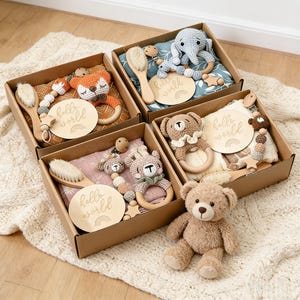 Może przedstawiać: Cztery pudełka z prezentami dla niemowląt z różnymi przedmiotami. Każde pudełko zawiera drewnianą szczotkę, szydełkową gryzak dla zwierząt, klips do smoczka i drewniany dysk z napisem "hello world" i tęczą. Pluszowy miś siedzi z przodu.