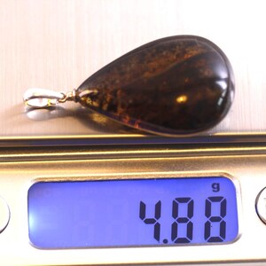 May include: A teardrop-shaped amber pendant with a silver bail, weighing 4.88 grams, on a digital scale.