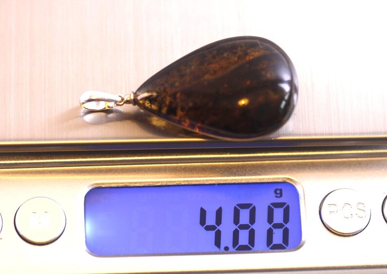 May include: A teardrop-shaped amber pendant with a silver bail, weighing 4.88 grams, on a digital scale.