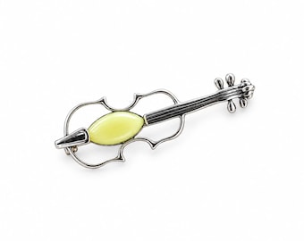 Op de afbeelding: Een zilverkleurige metalen broche in de vorm van een viool, met een open frameontwerp en een gladde, lichtgele, ovaalvormige inleg in het midden van de body. Het sieraad heeft gedetailleerd krulwerk bij de kop en een textuur op de hals.