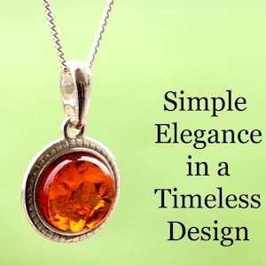 Puede incluir: Un collar con colgante de plata con una piedra redonda de color ámbar. La piedra está engastada en un bisel de plata y cuelga de una delicada cadena de plata. El fondo es verde claro. Texto: Simple Elegancia en un Diseño Atemporal.