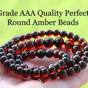 May include: A collection of round amber beads in shades of brown and red. The beads are strung together, possibly for a necklace or bracelet. The image includes the text "Grade AAA Quality Perfect Round Amber Beads".